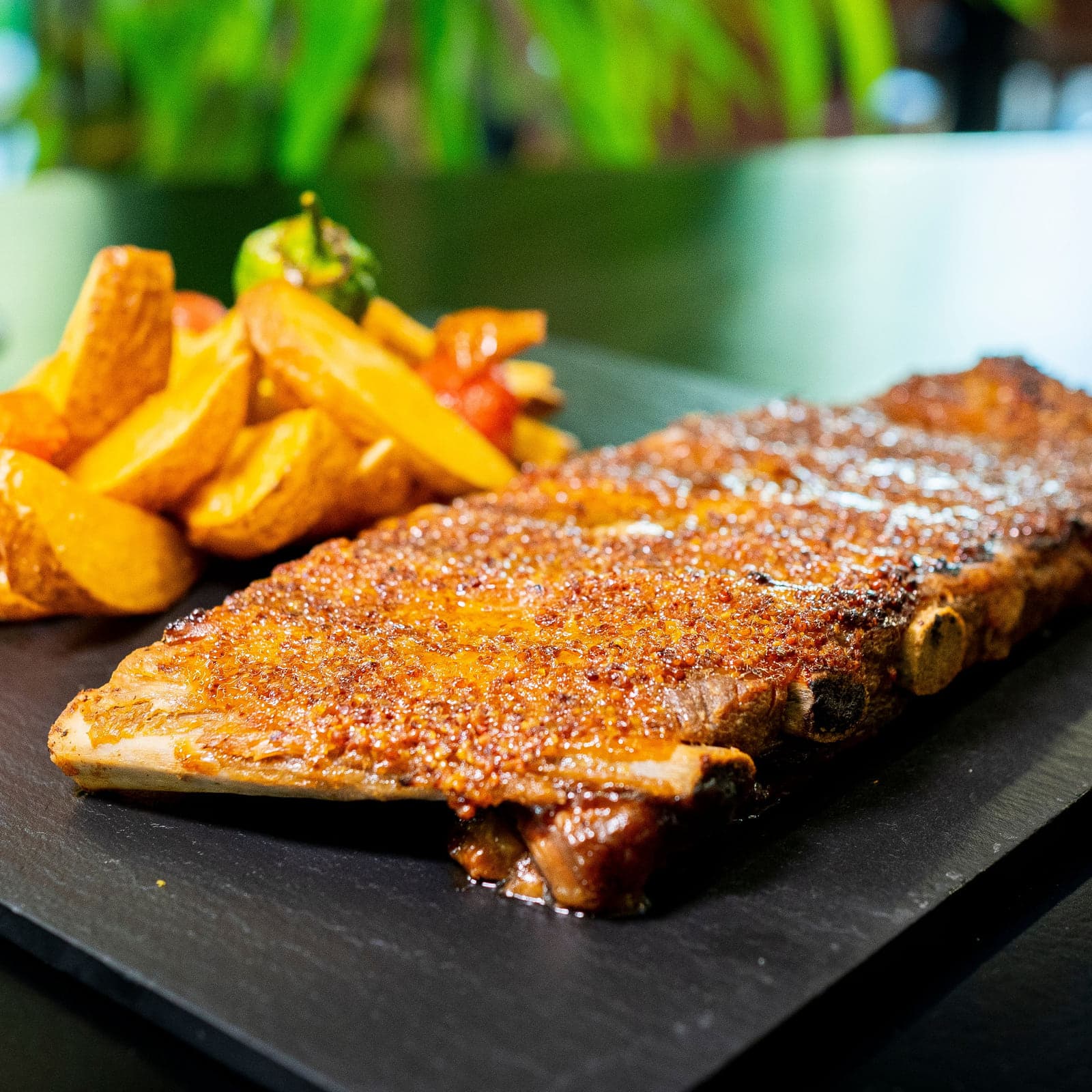 Costillar sobre pizarra con patatas, tomates cherry y pimiento verde