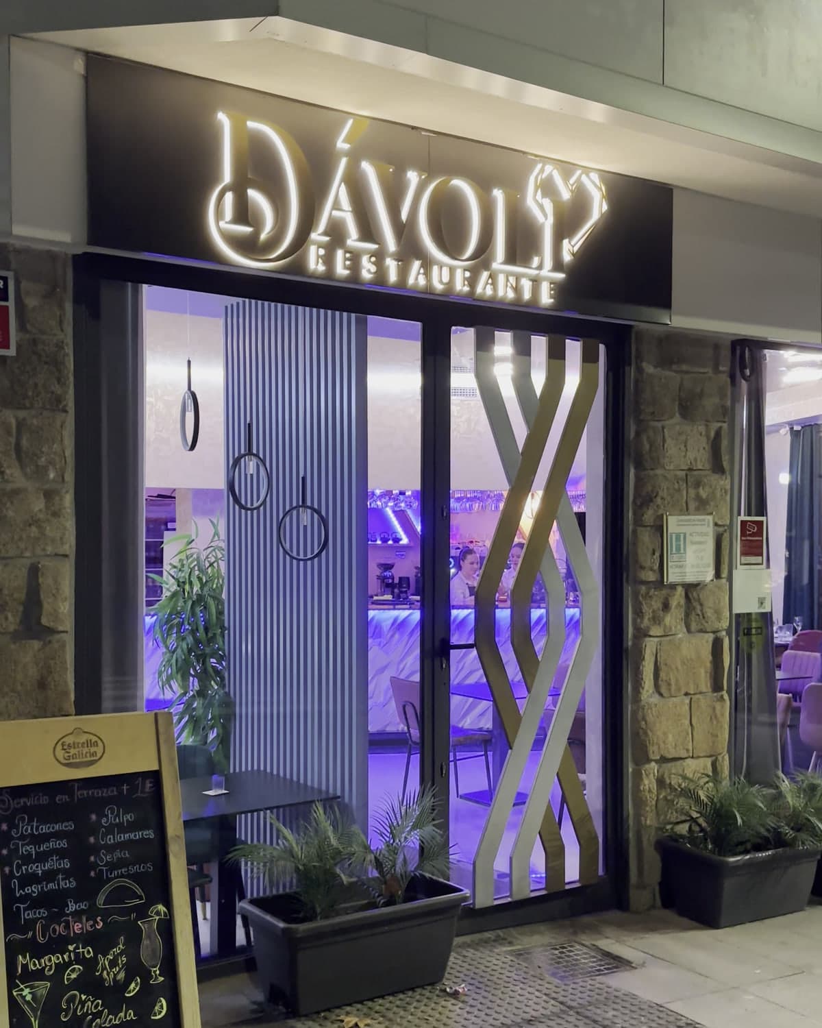 La entrada de Dávoli de noche, con el rótulo encendido y la pizarra en la puerta
