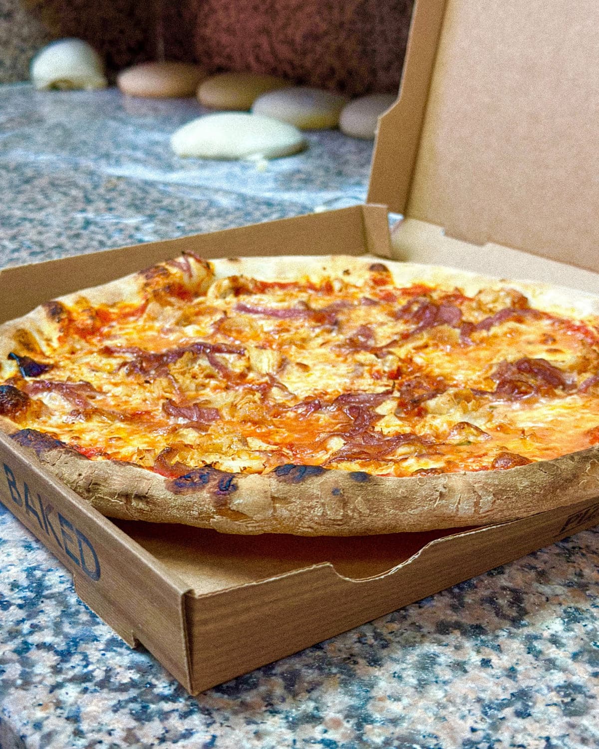 Pizza en su caja para llevar, con bolas de masa detrás