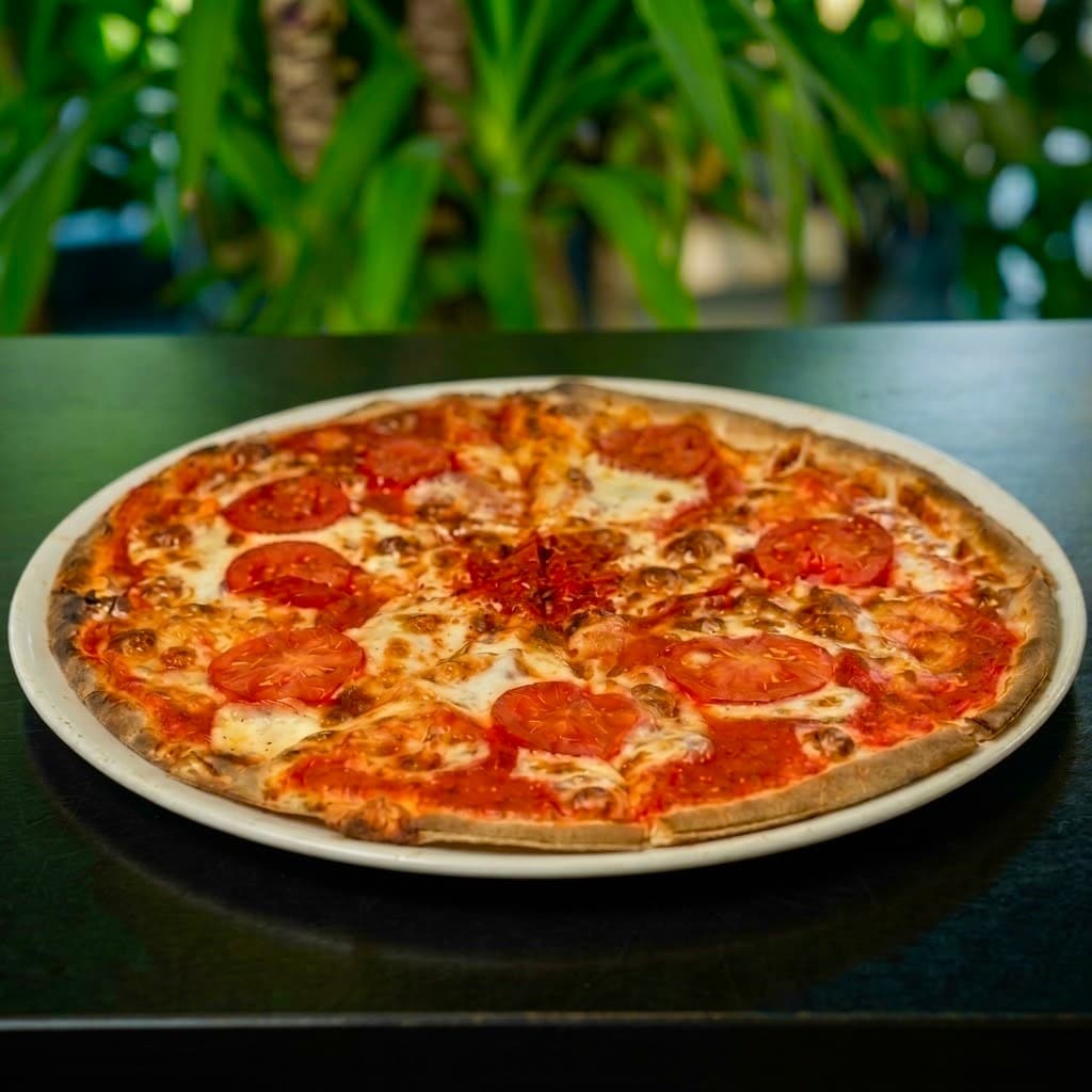Pizza con rodajas de tomate y queso fundido en un plato blanco