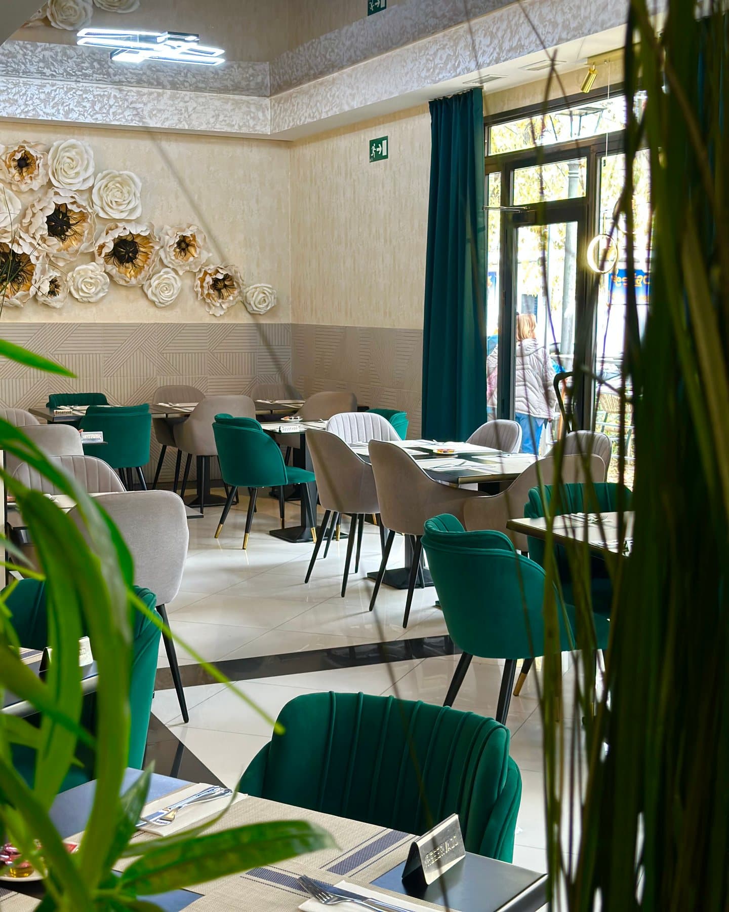 La sala, con sillas verdes y grises, mesas negras y flores de papel en la pared