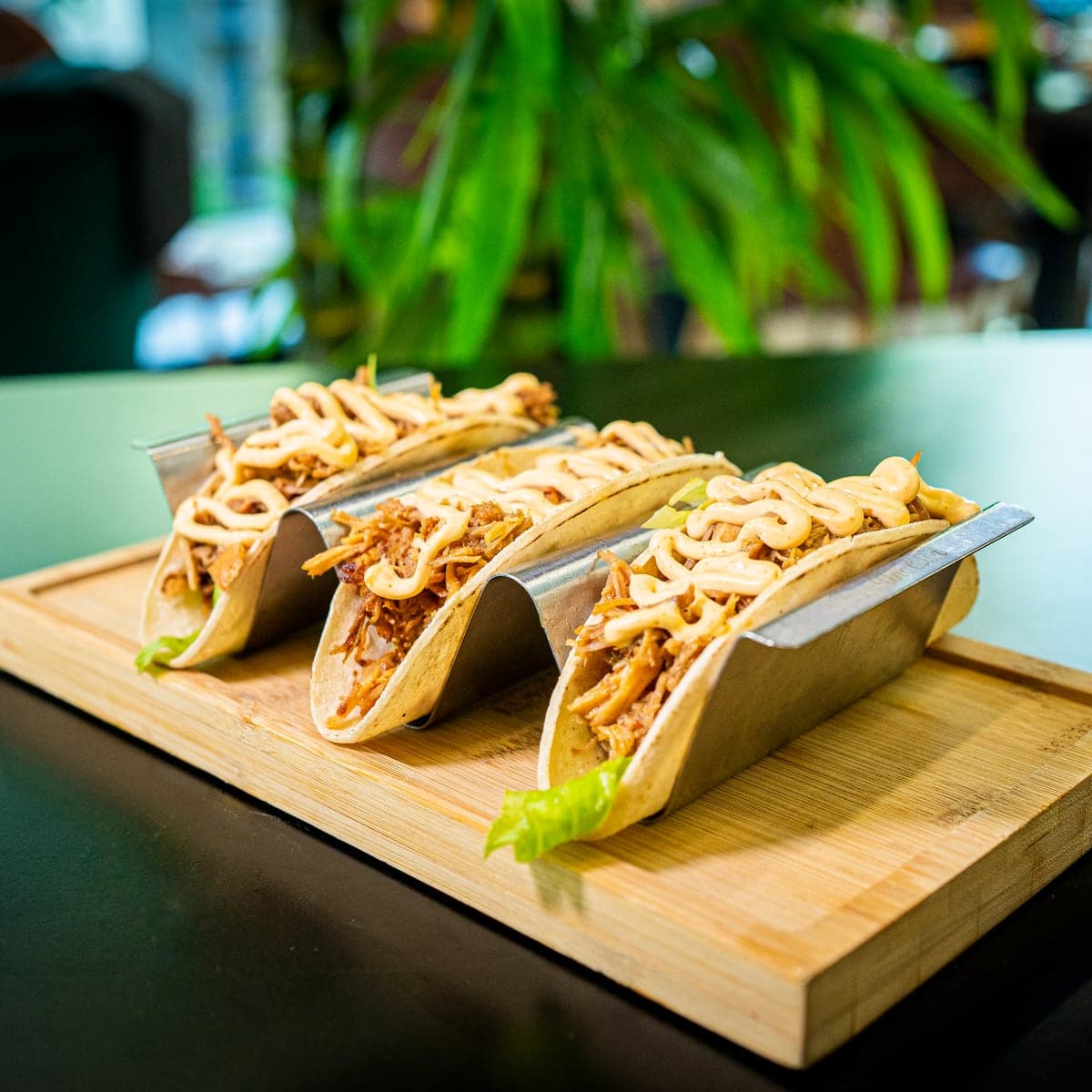 Tres tacos de cochinita pibil en su soporte, sobre una tabla de madera