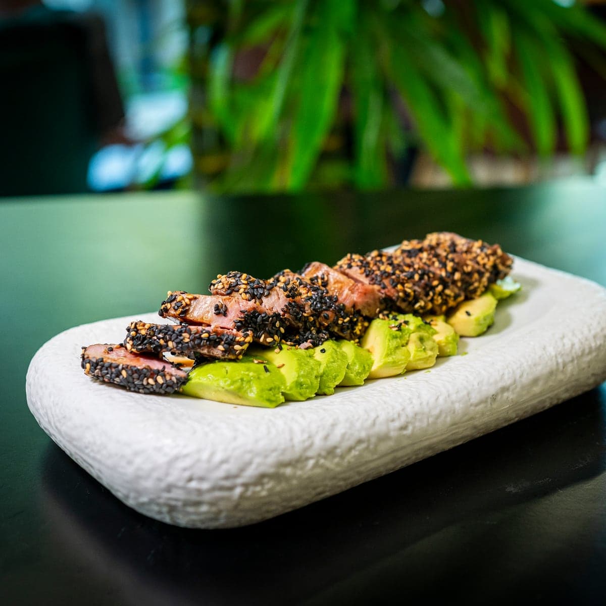 Tataki de atún con sésamo sobre aguacate, en una bandeja blanca
